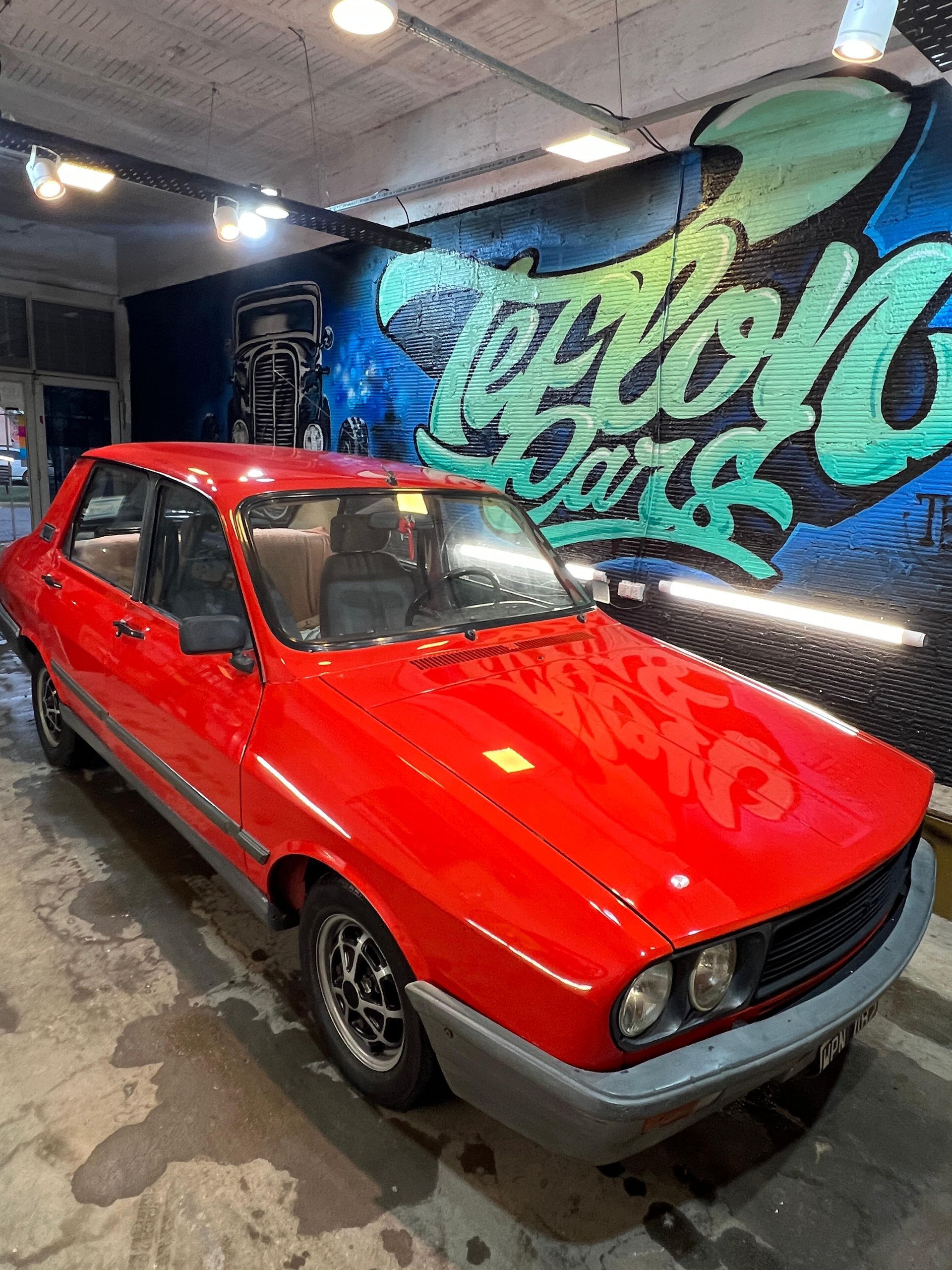 Coche antiguo rojo aparcado en un garaje con grafitis en la pared.
