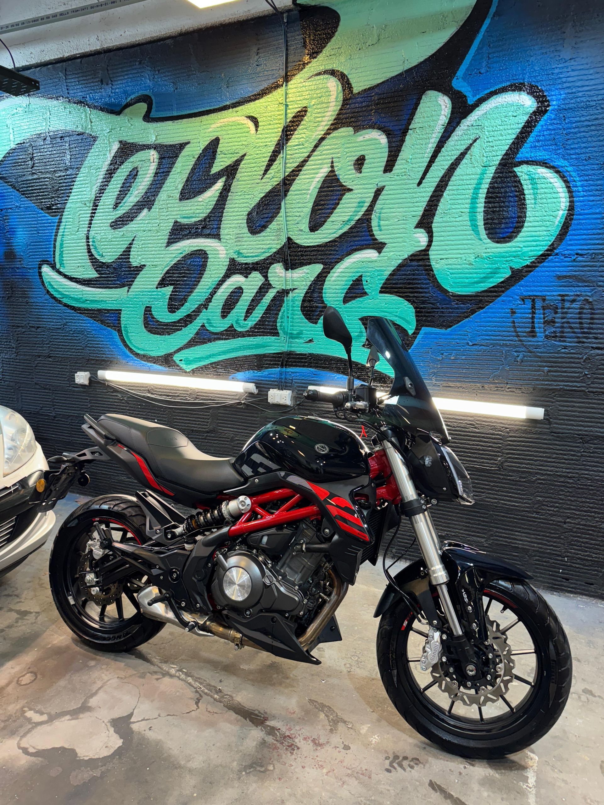 Motocicleta Benelli negra y roja estacionada frente a una pared con grafitis que dicen 