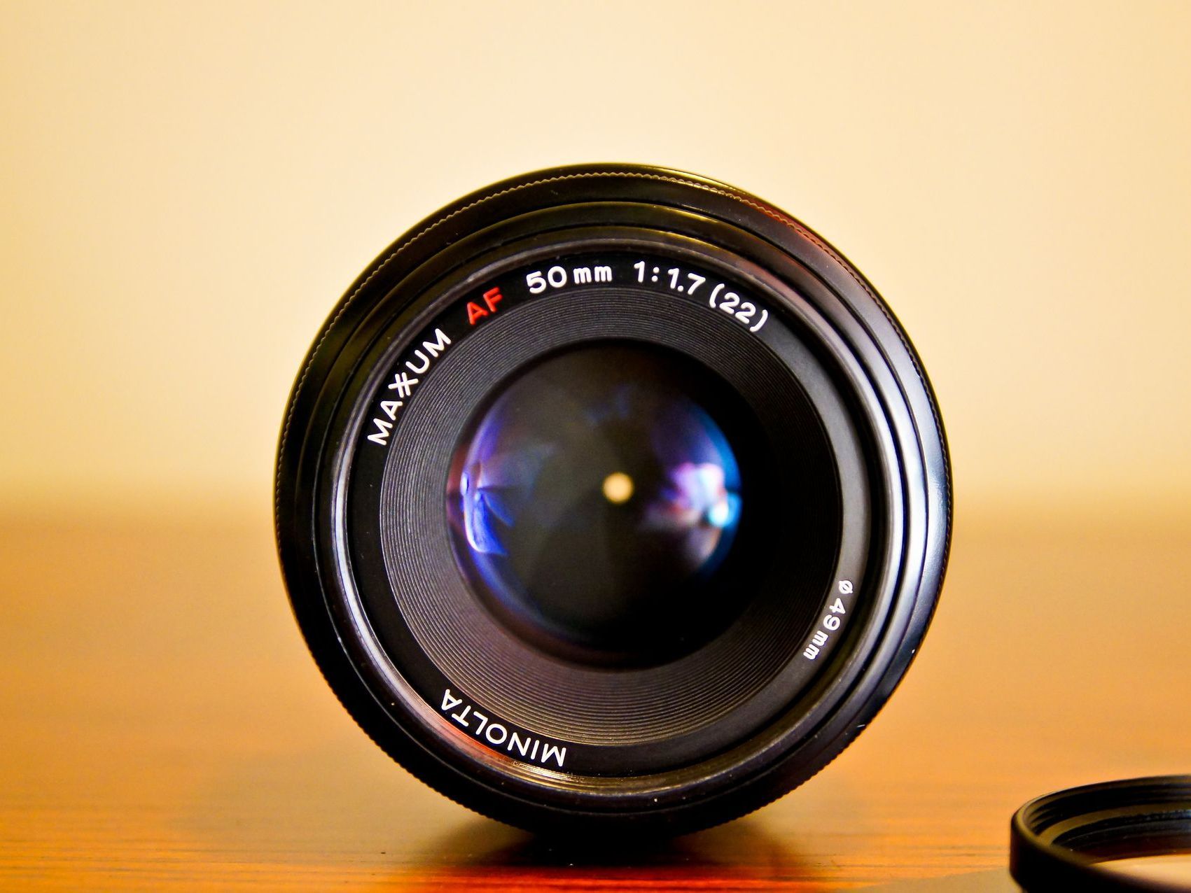 Camera lenses image, preowned camera lens facing  camera on wooden table with yellow wall out of focus in background