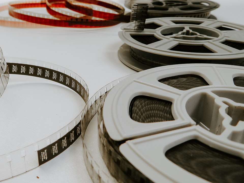 Movie Film Transfer image, several movie film reels on a white surface, with film unspooled