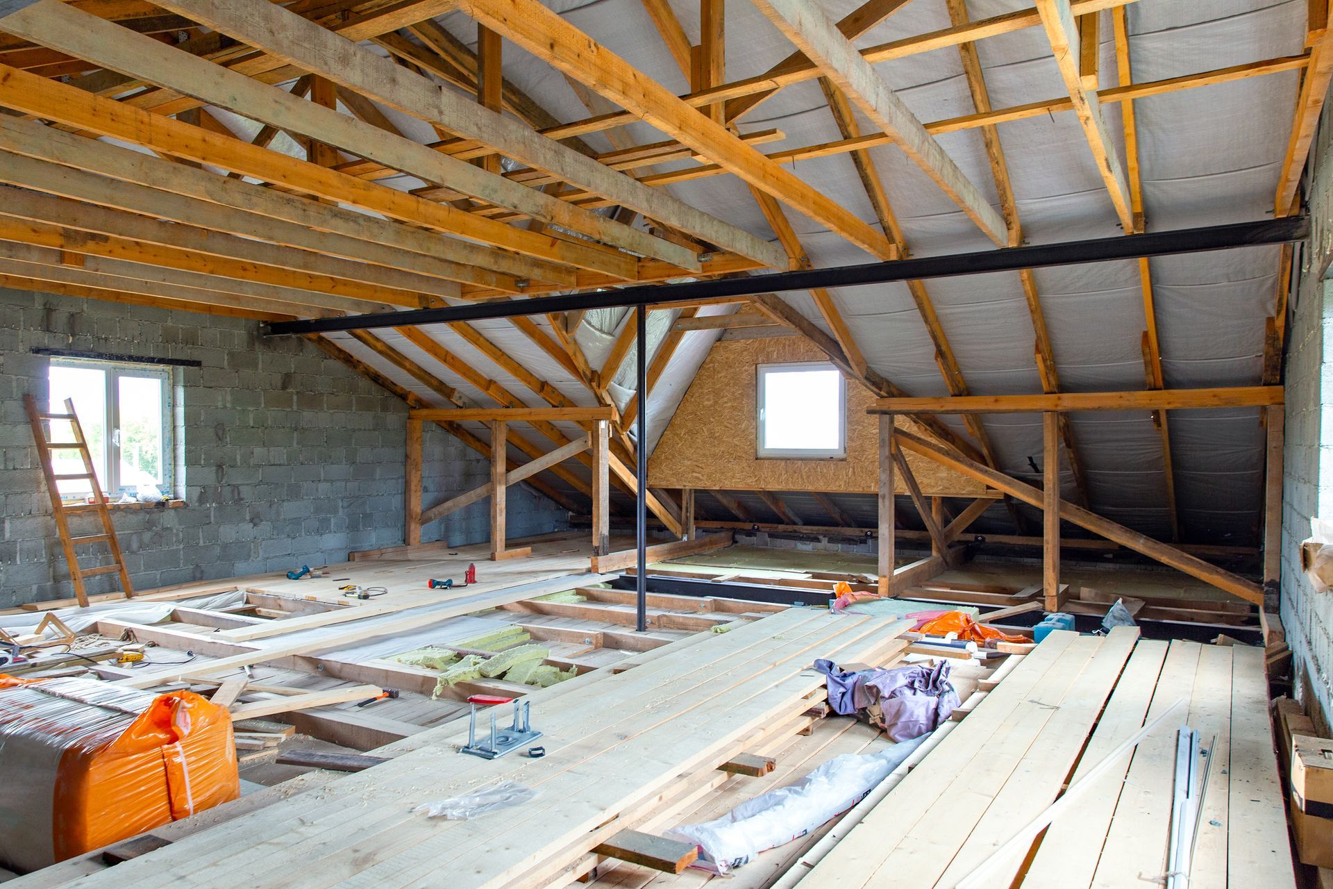 An attic under construction with wooden beams and a ladder.