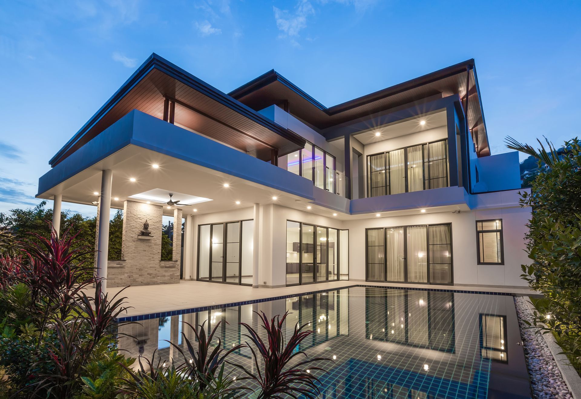 Modern multi-story house with pool, evening lighting, reflecting windows.