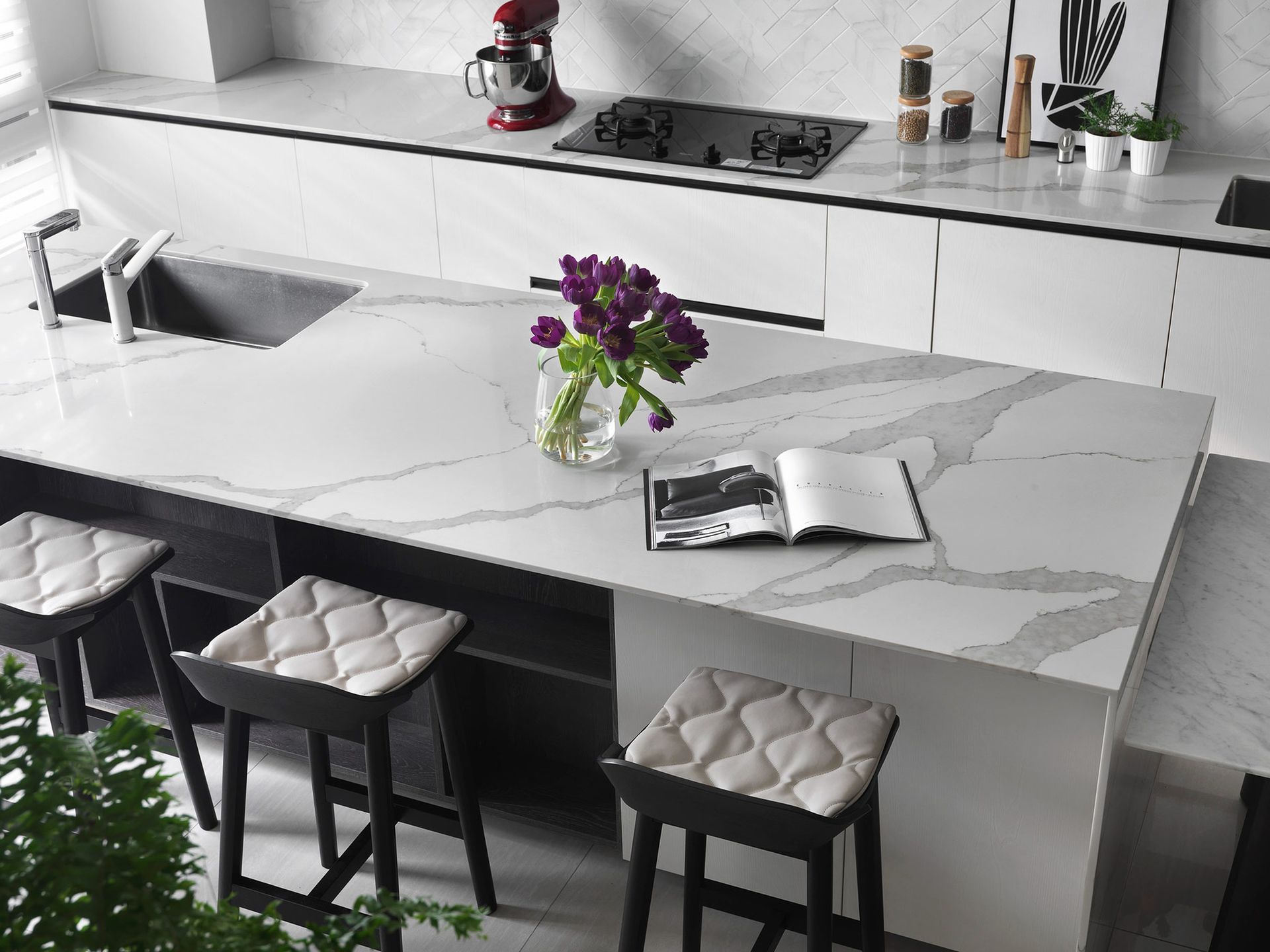 Modern kitchen with white marble countertop, purple flowers, and stools.