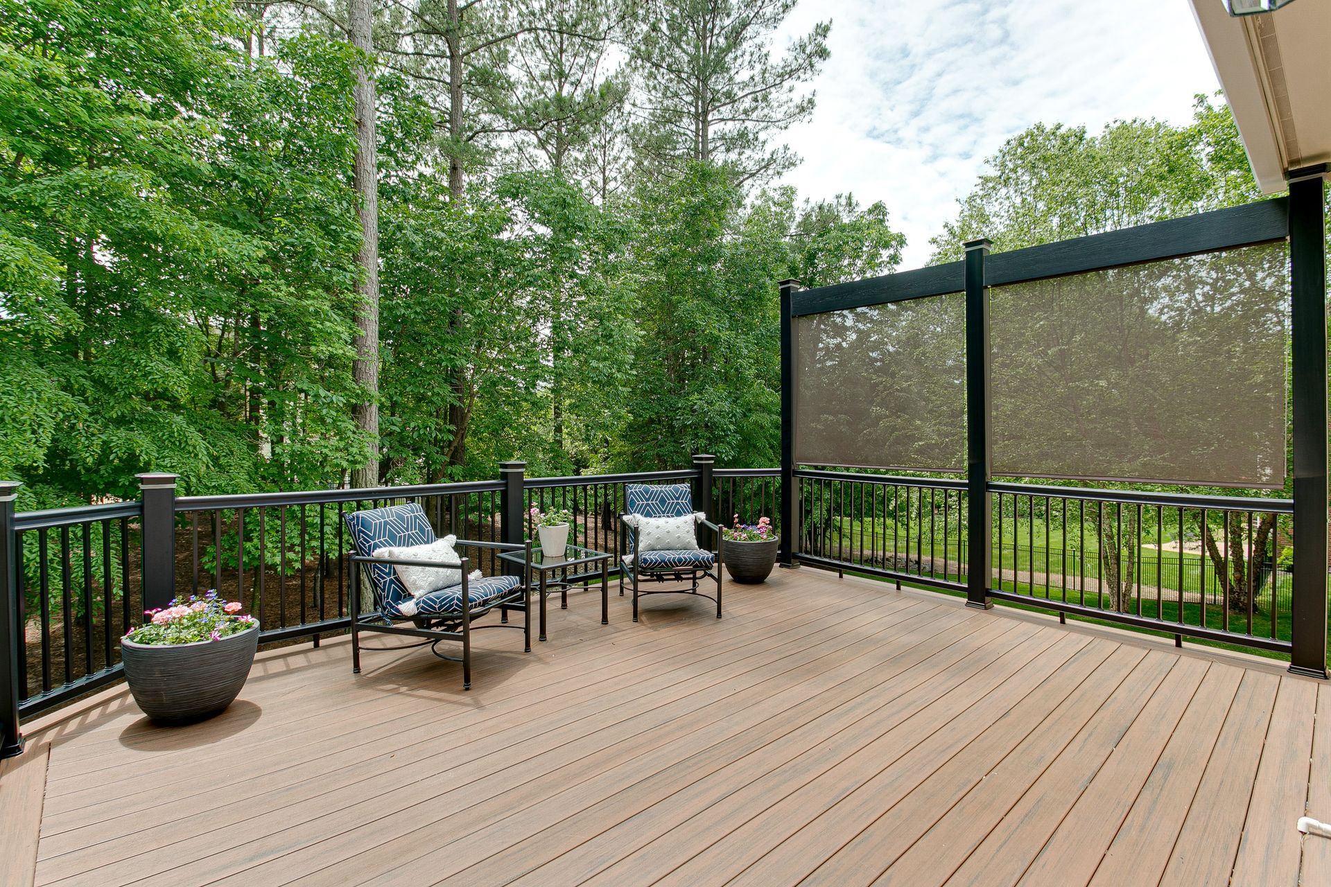 Outdoor wooden deck with chairs, table, potted plants, and view of trees.
