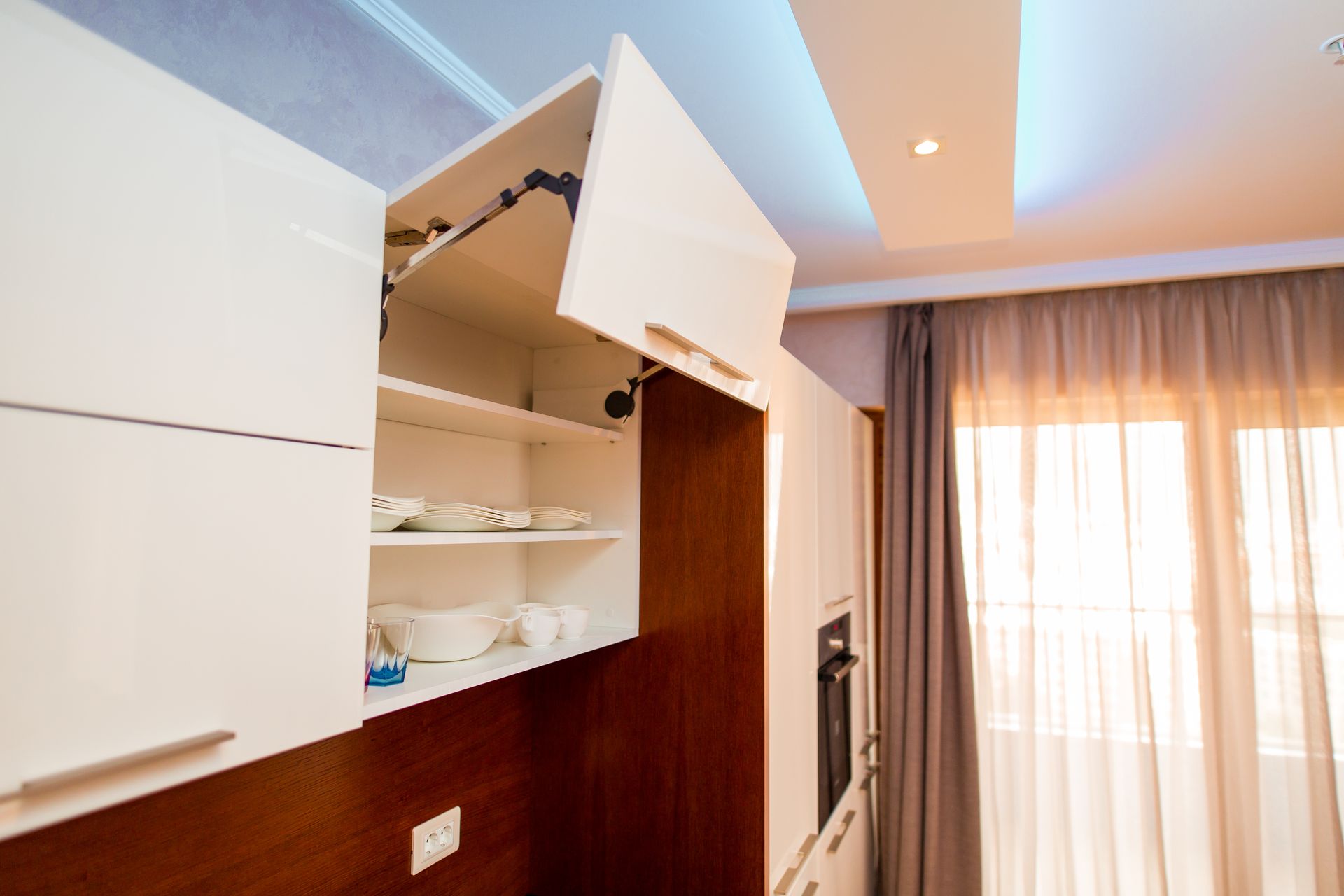 Modern kitchen cabinet open, displaying stacked dishes and cups inside.
