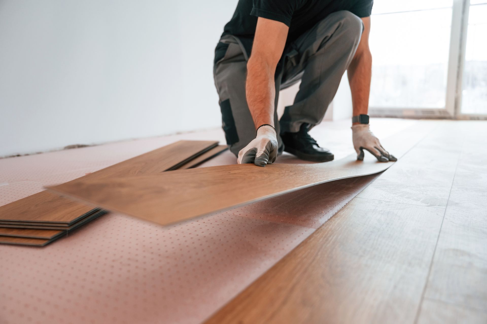 Person installing wood laminate flooring in a room.