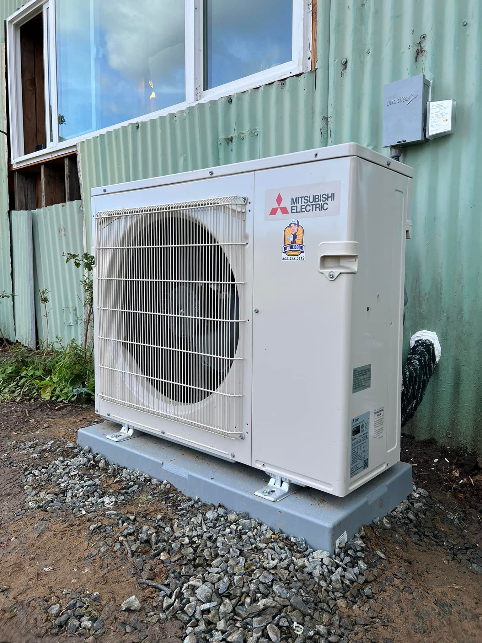 A white air conditioner is sitting on top of a pile of gravel in front of a building.