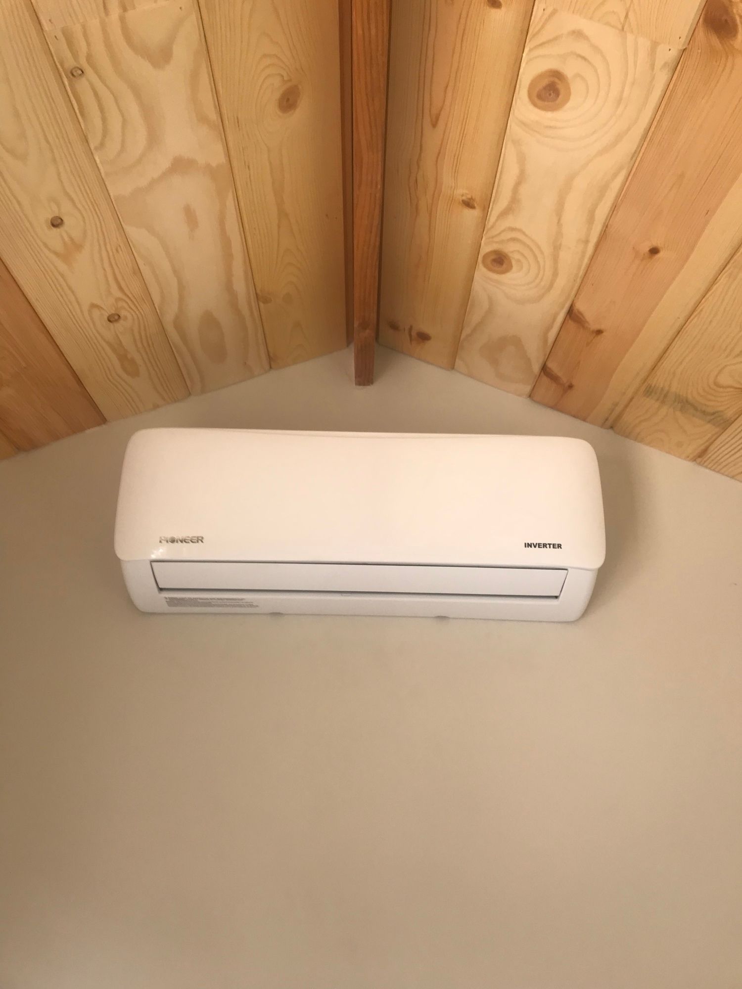 A white air conditioner is mounted on a wall in a room with wood paneling.