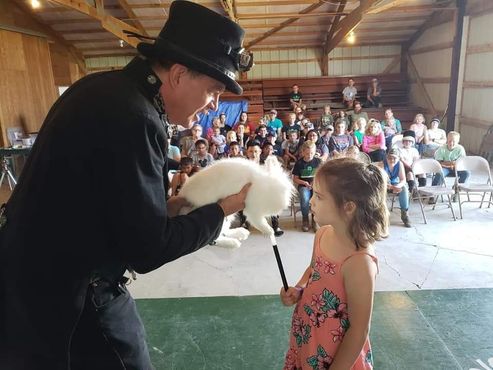 A man in a top hat is holding a white rabbit in front of a little girl.