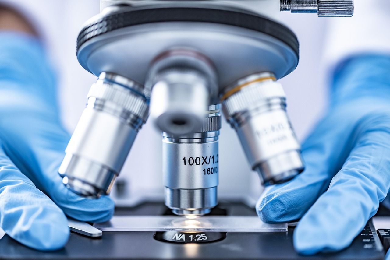 A person wearing blue gloves is looking through a microscope.