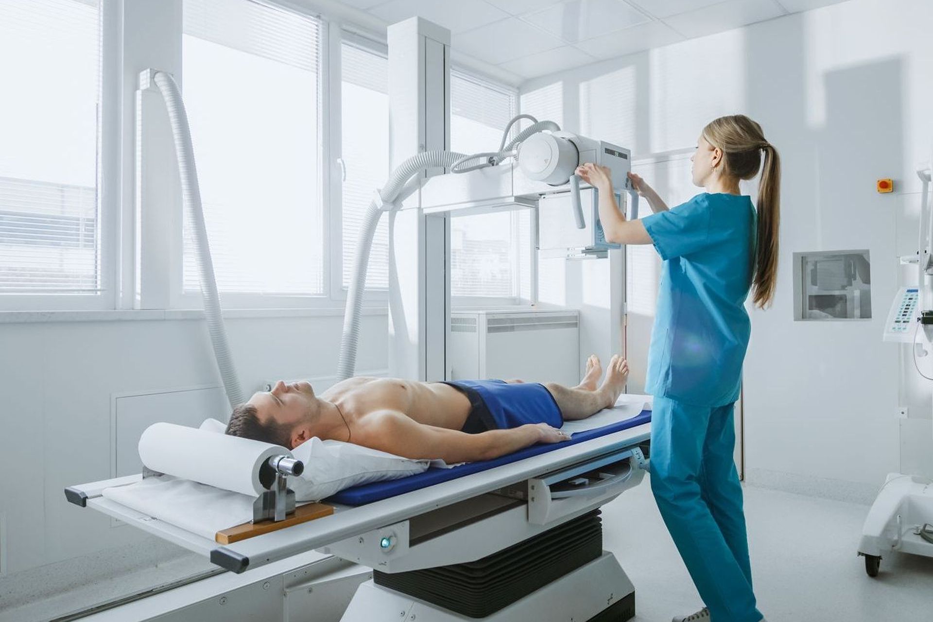 A nurse is taking an x-ray of a man laying on a bed.