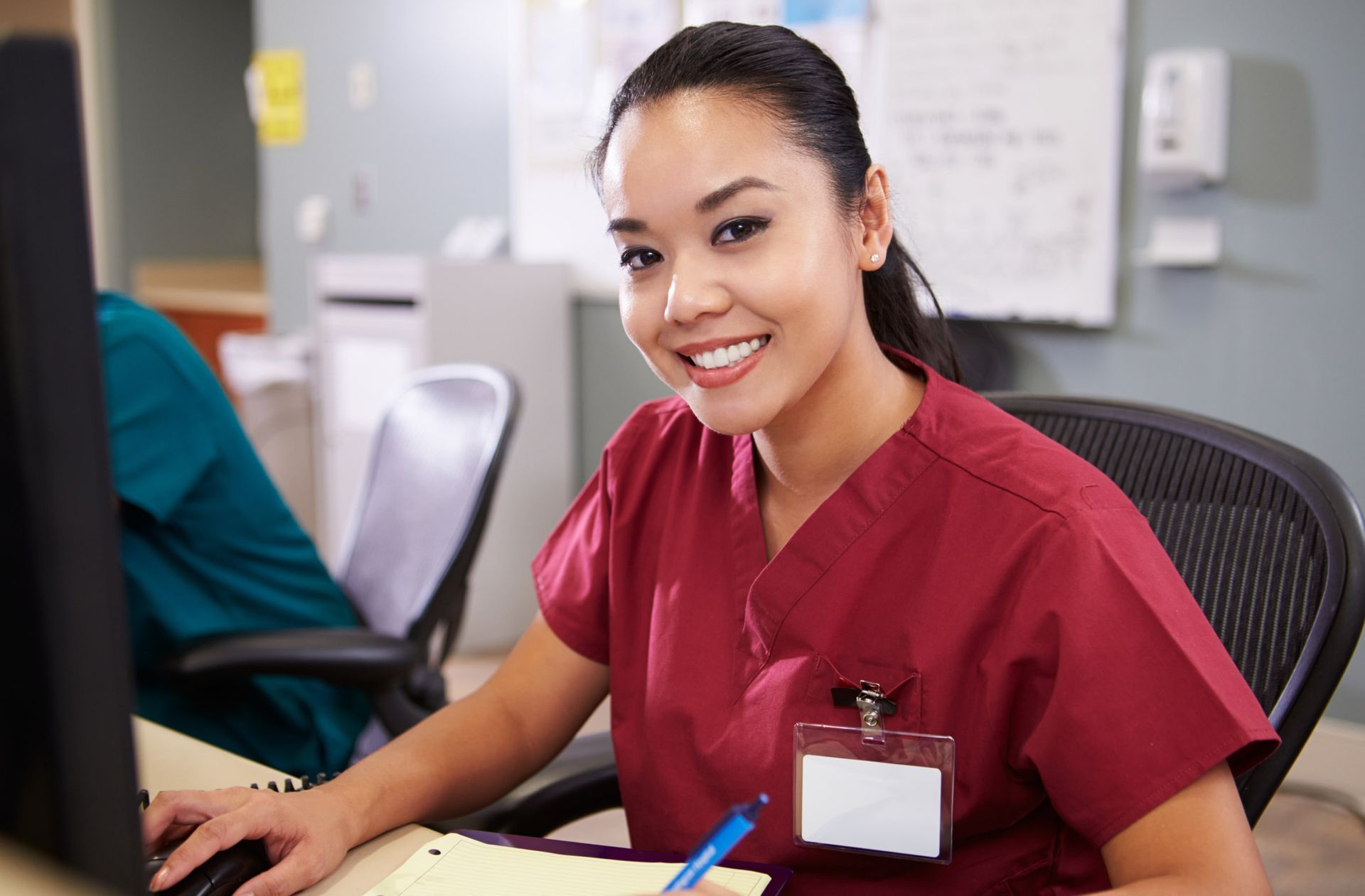 A nurse is smiling while sitting at a desk in front of a computer.
