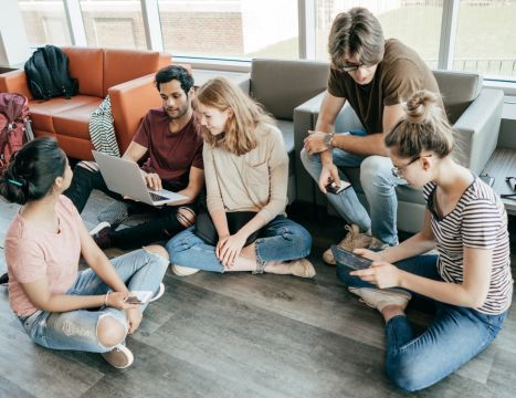 A group of young people are sitting on the floor in a living room.