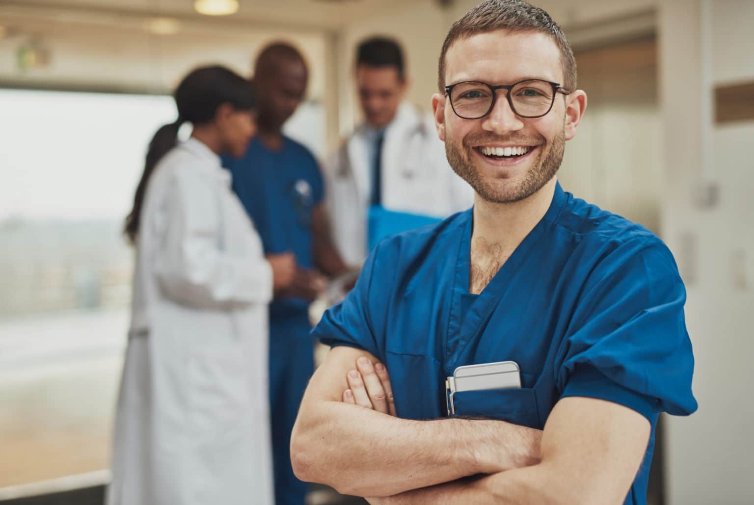 A nurse is smiling with his arms crossed in front of a group of doctors.