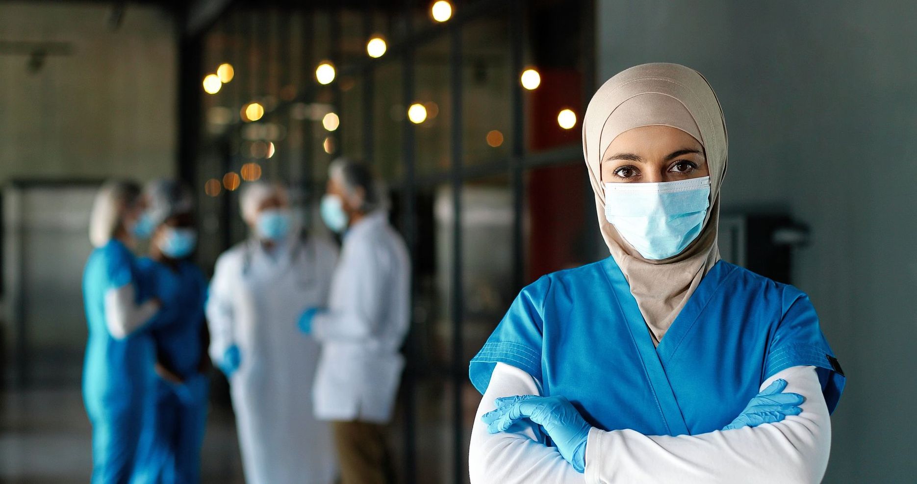 A nurse wearing a mask and gloves is standing in front of a group of doctors.