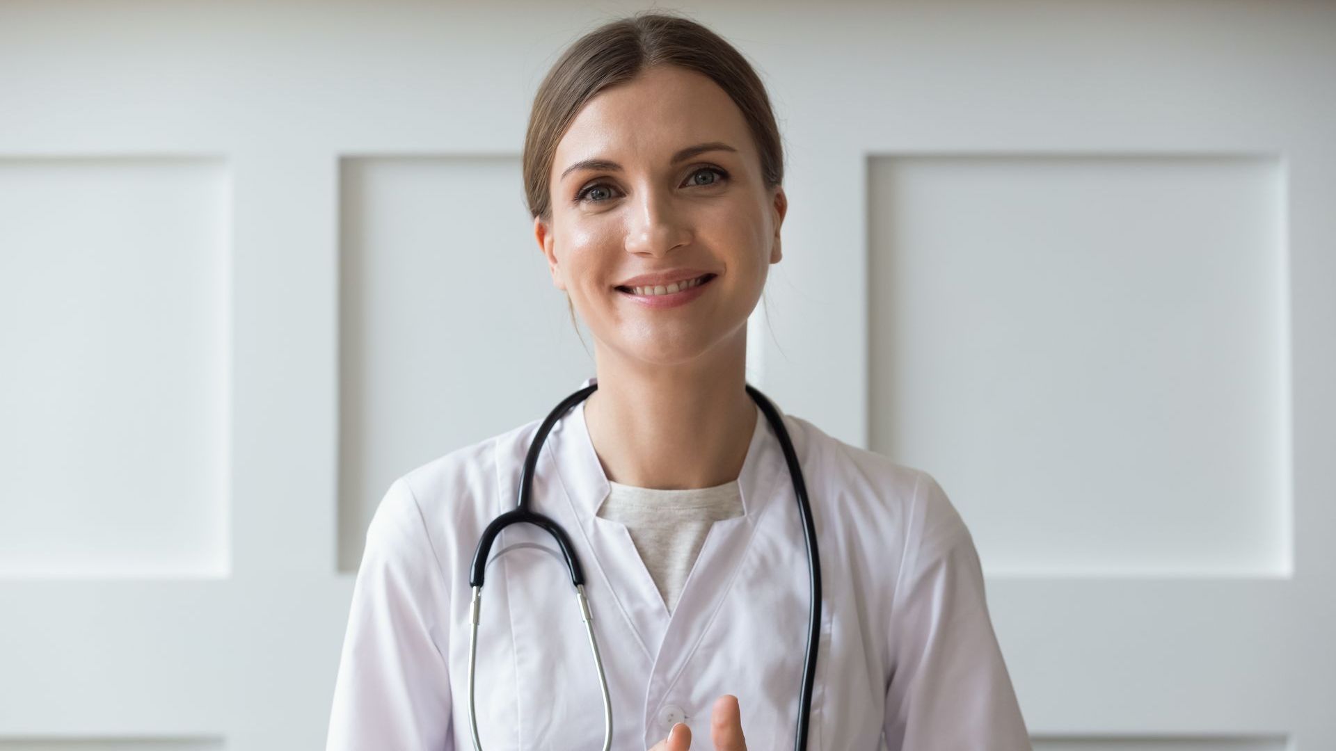A female doctor with a stethoscope around her neck is smiling while sitting on a couch.