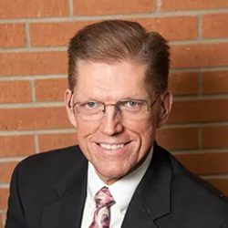 A man in a suit and tie is smiling in front of a brick wall.