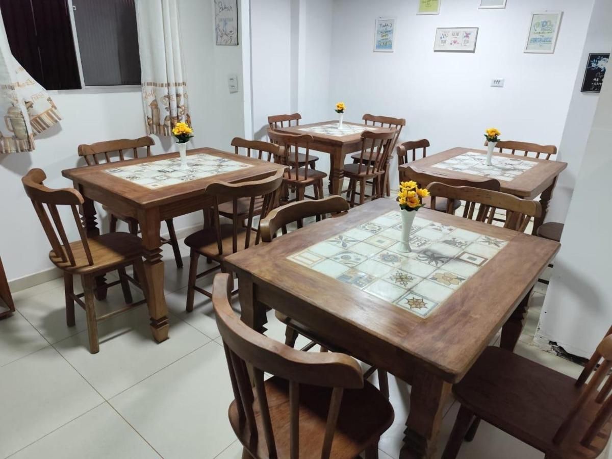 Mesas e cadeiras de madeira em uma sala de jantar, cada uma com um vaso de flores amarelas.