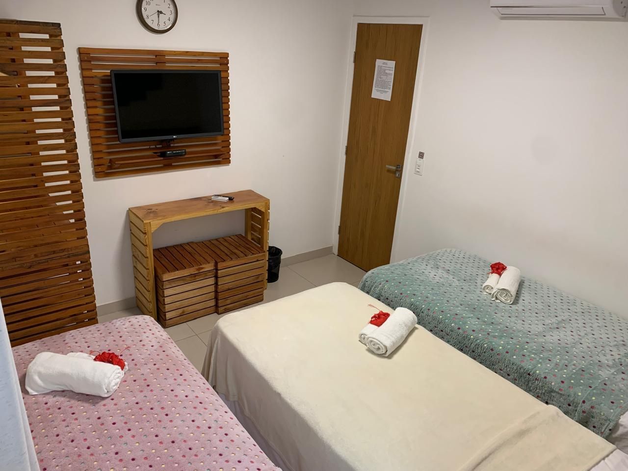 Uma pequena sala de spa com três mesas de massagem, uma TV e detalhes em madeira.