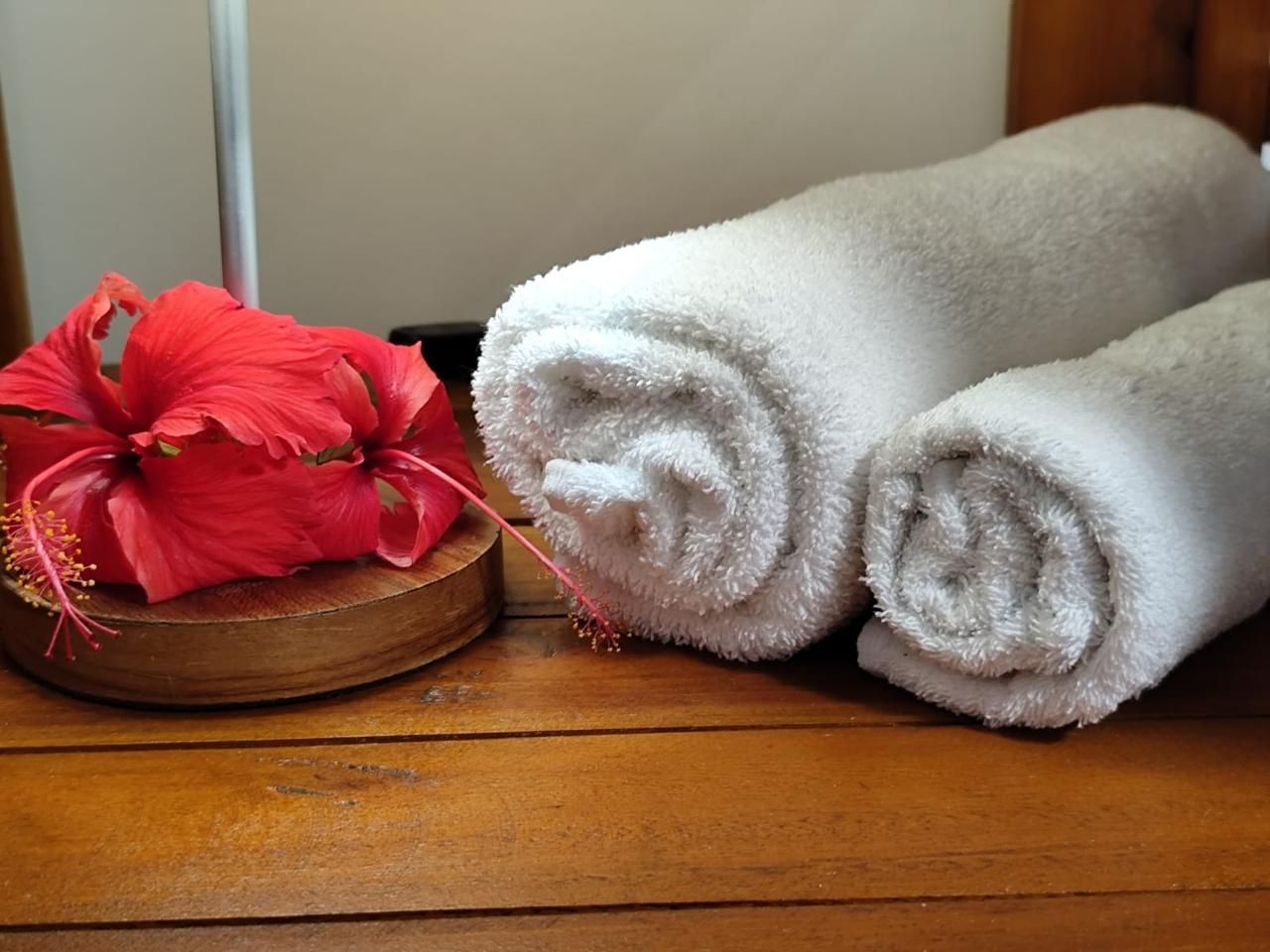 Toalhas brancas enroladas e uma flor de hibisco vermelha sobre uma superfície de madeira.