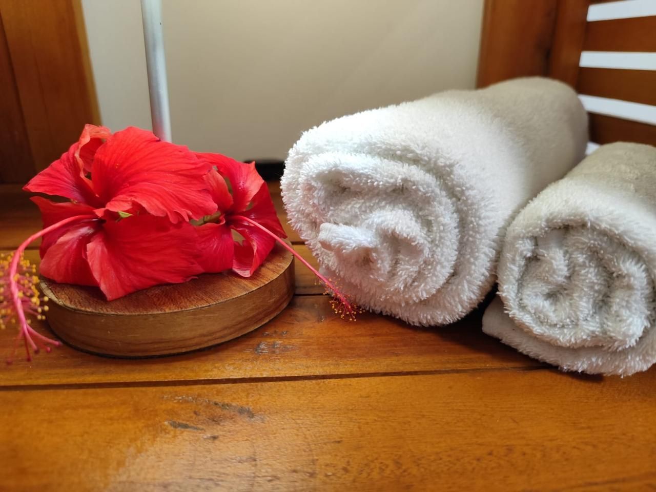 Toalhas brancas enroladas e uma flor vermelha sobre uma prateleira de madeira.