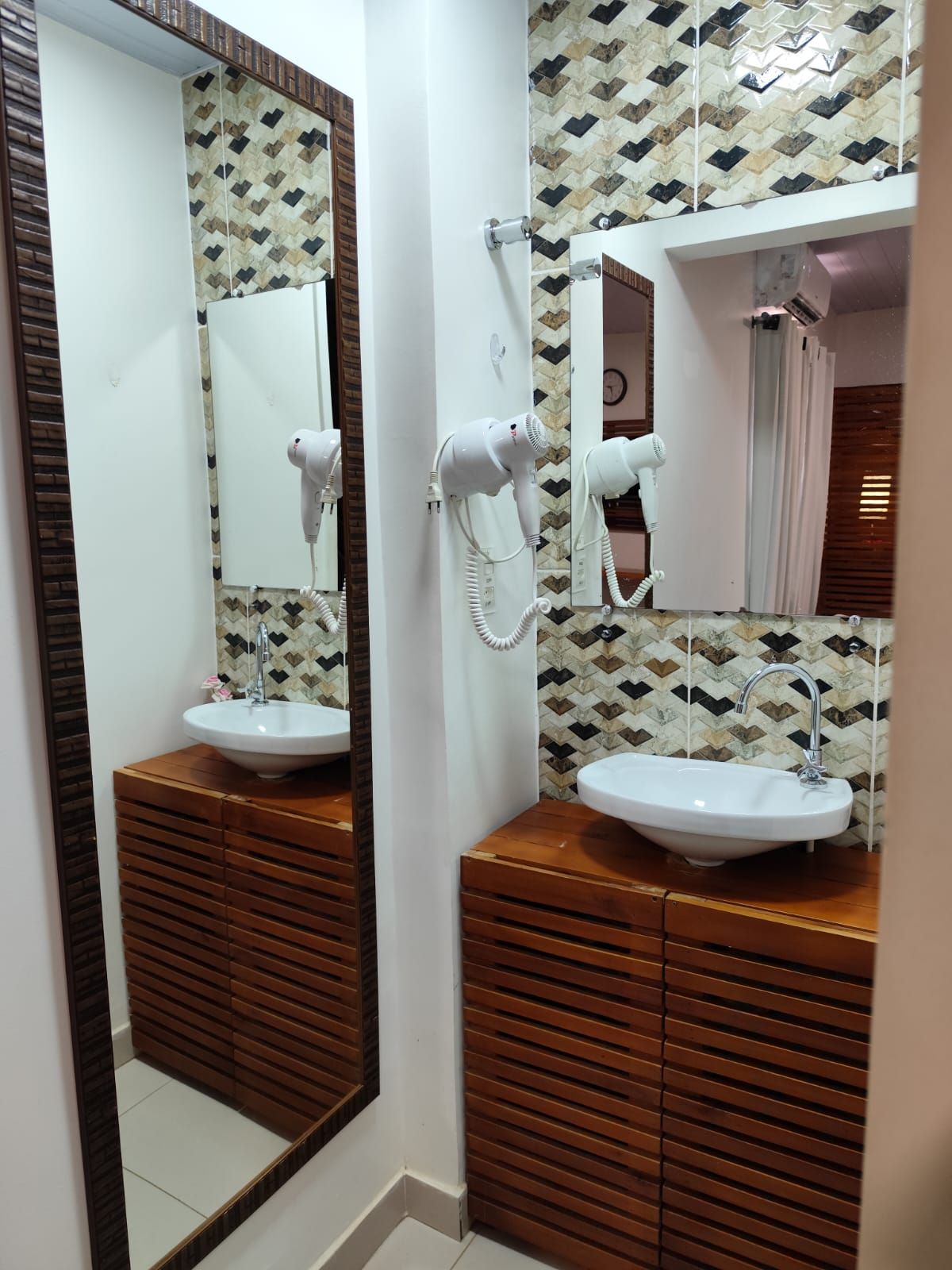 Banheiro com duas pias, armários de madeira, backsplash de azulejos estampados e grandes espelhos.