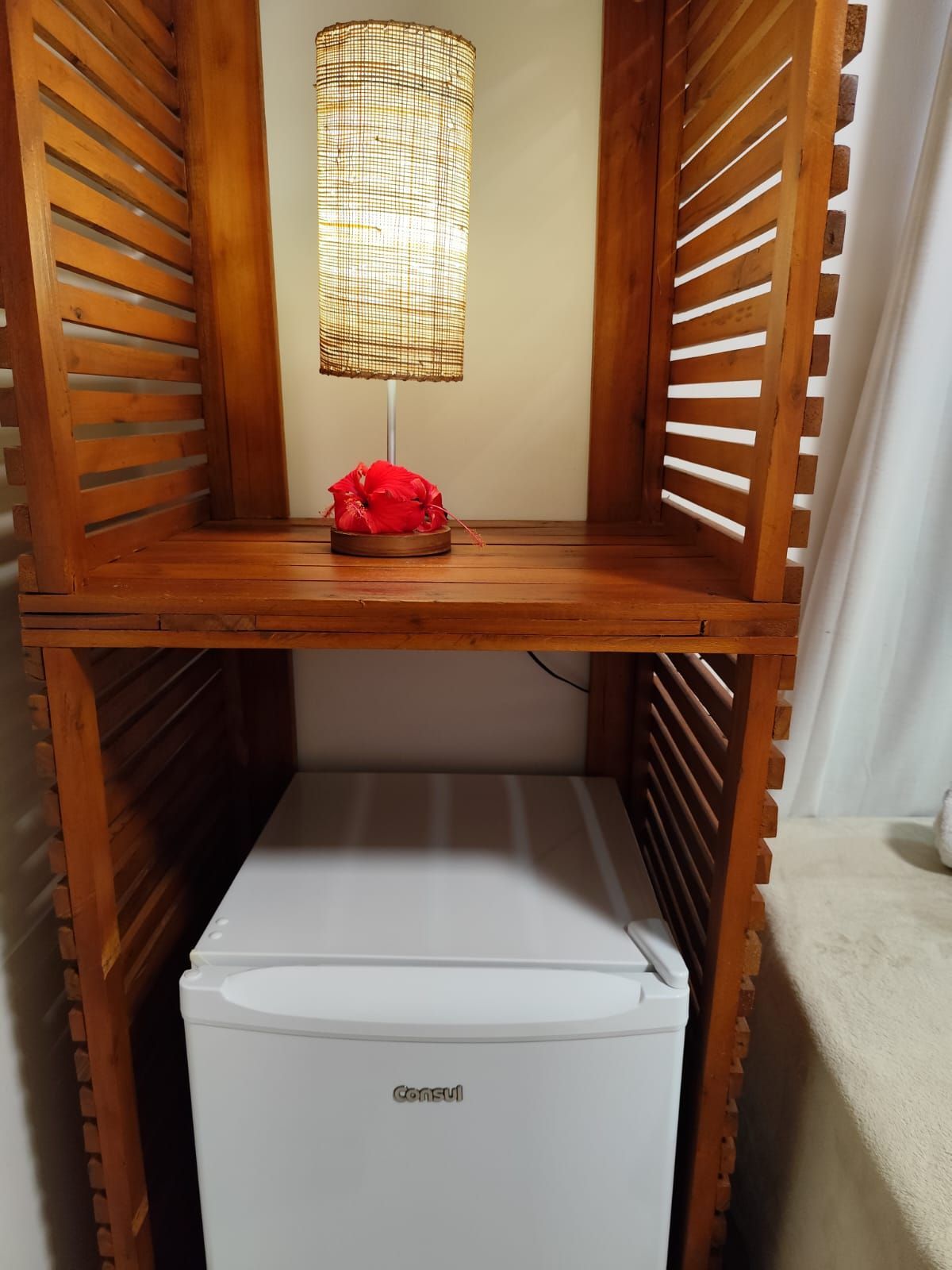 Estante de madeira com frigobar, luminária e objeto decorativo vermelho.