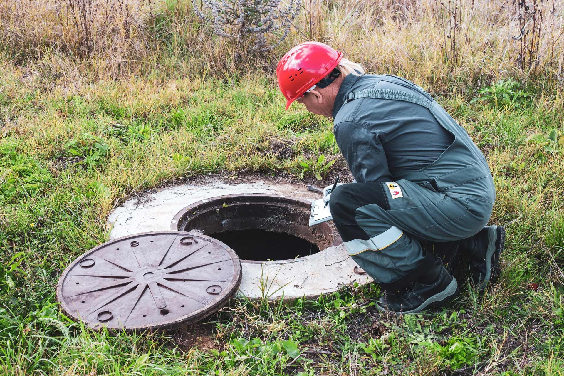 Person in jumpsuit and helmet inspecting a well