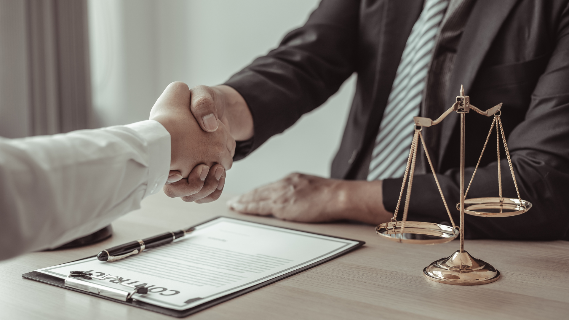 Two people shaking hands over a contract on a desk, with a scale of justice.