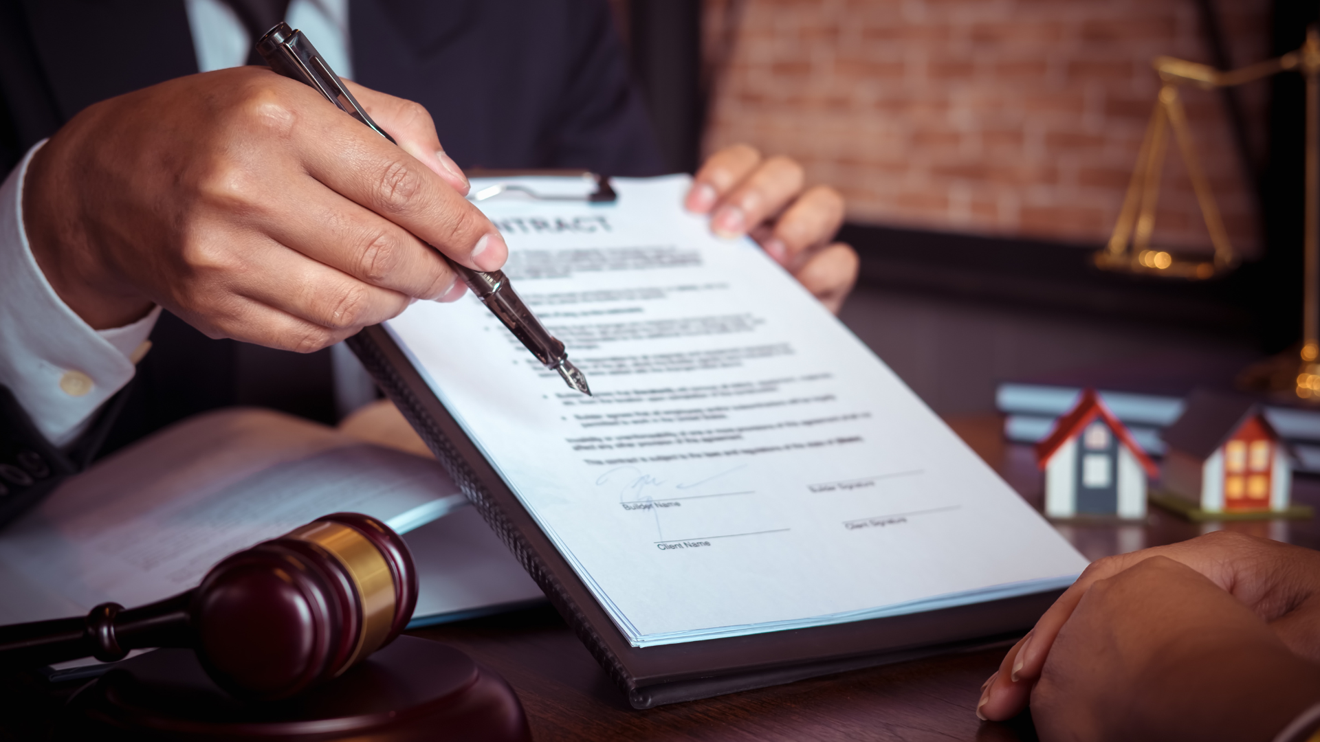 Person in suit points to contract on clipboard with gavel and scales in background.