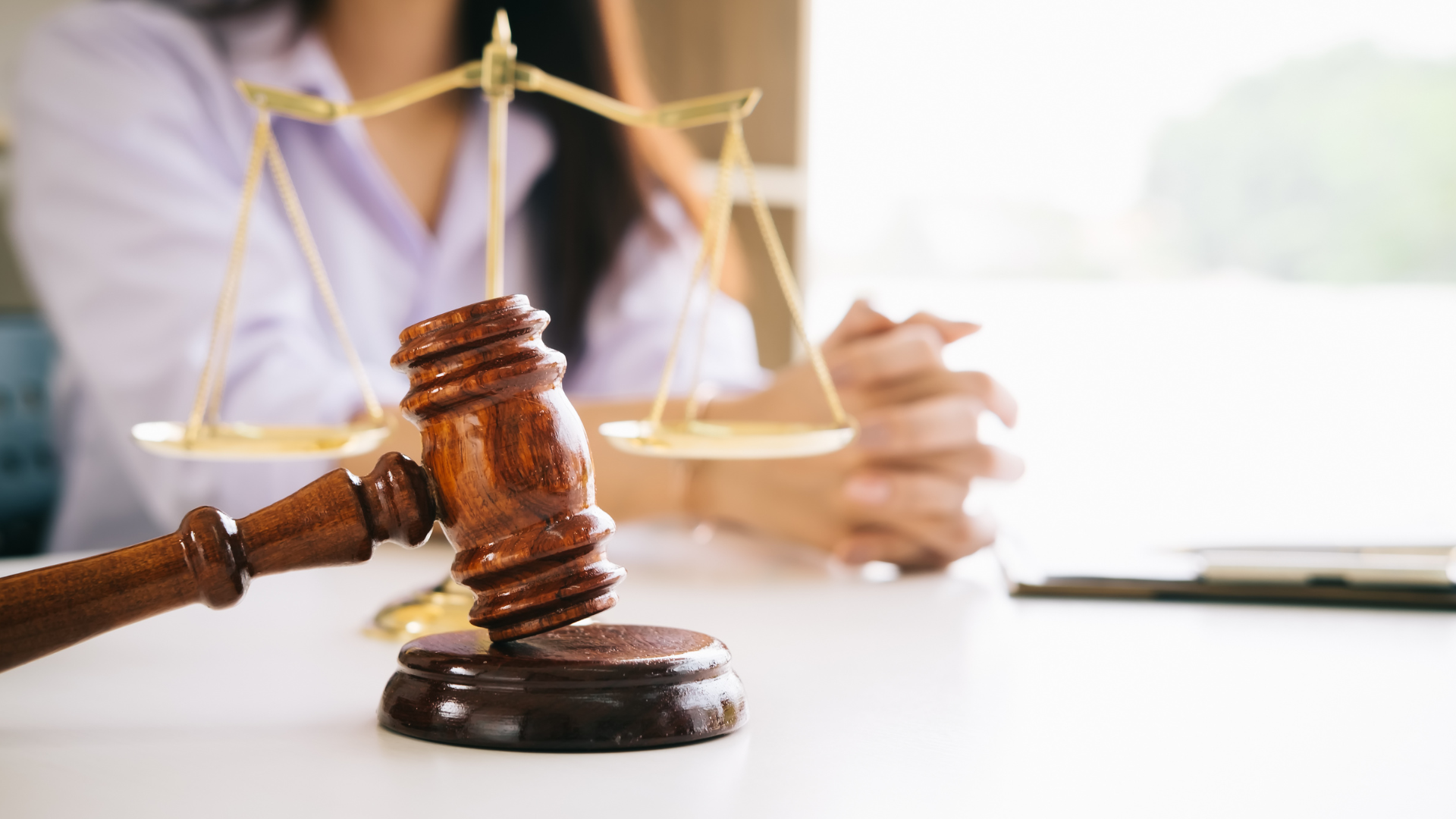 Gavel on table in front of scales of justice and person in white shirt.