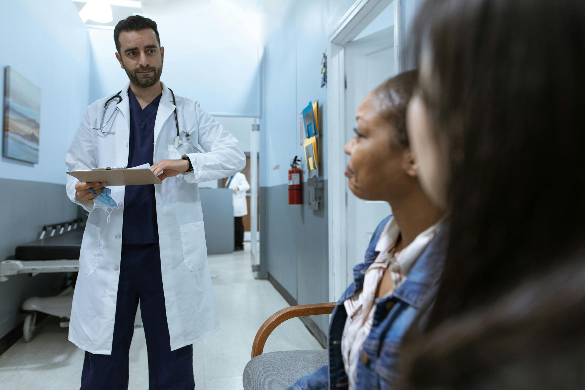 Doctor in white coat and scrubs talking to two patients in a hospital hallway.