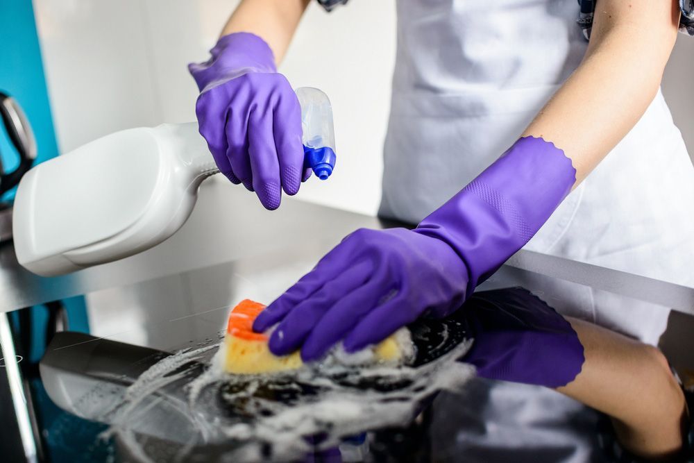 Woman's Hands Cleaning Kitchen Top In Rubber Protective Gloves — Jamac Cleaning Services in Merewether, NSW