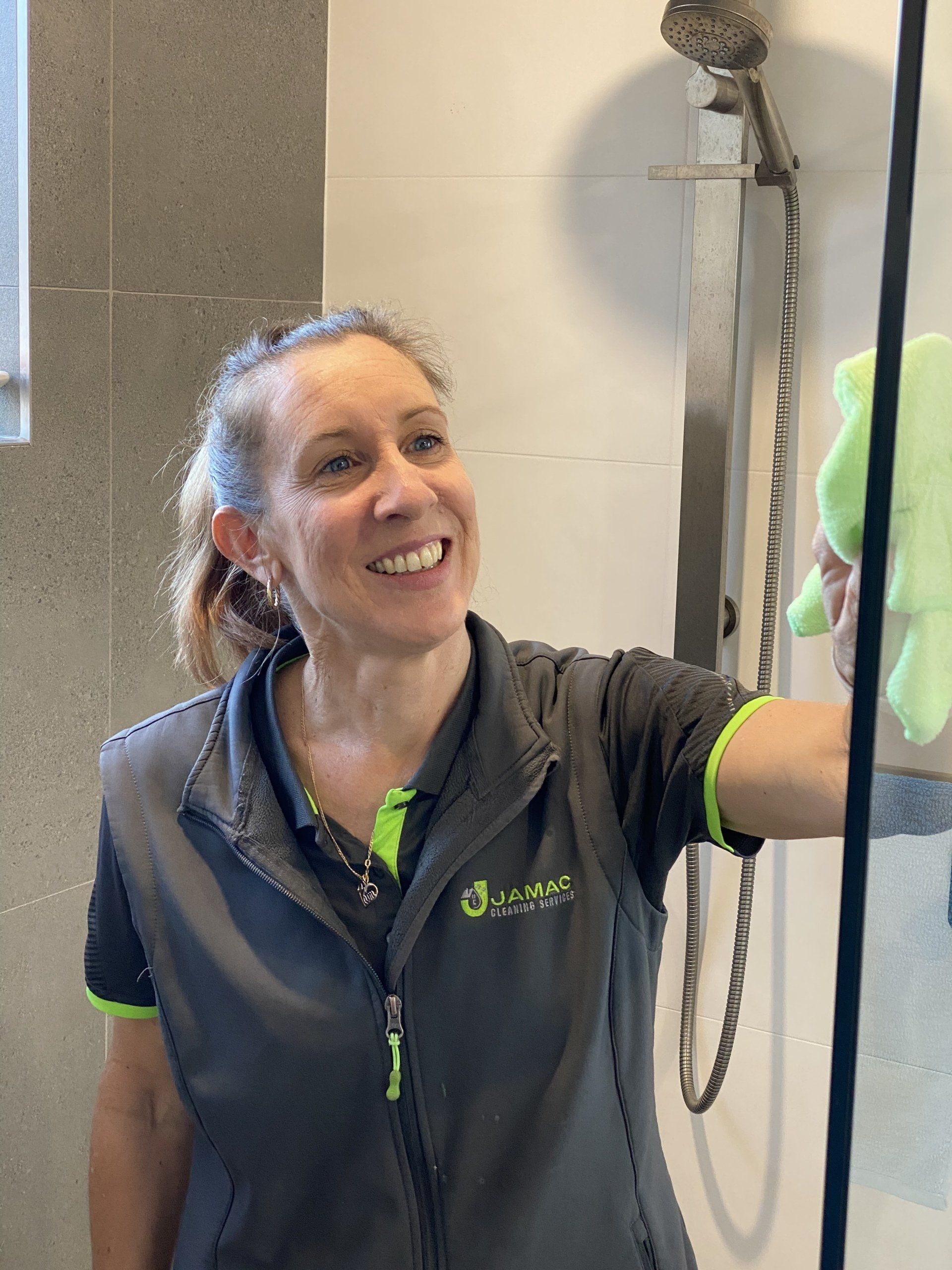 Smiling Lady Cleaning Shower — Jamac Cleaning Services in Cardiff, NSW