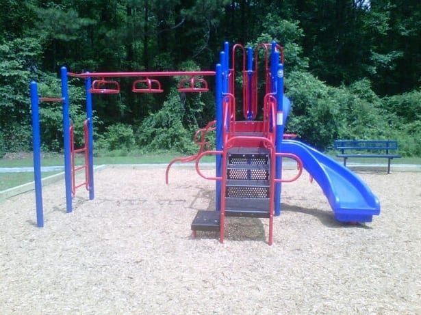 Playground with blue and red equipment on wood chips. Slide, bars, and steps.