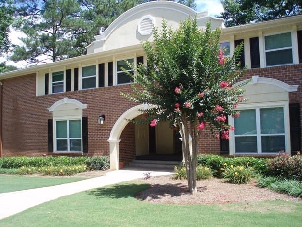 Two-story brick building with white trim, arched doorway, and flowering tree in front.