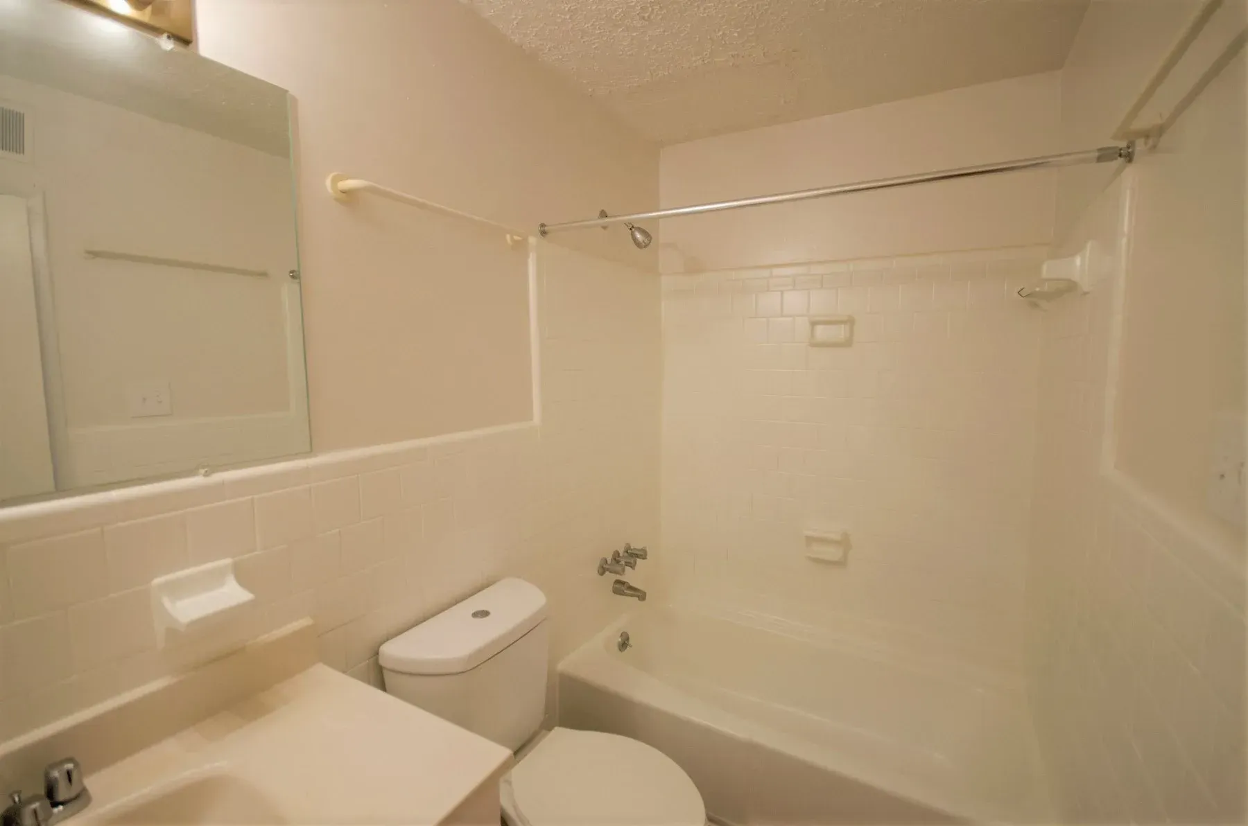 White bathroom with a bathtub, toilet, sink, and mirror.
