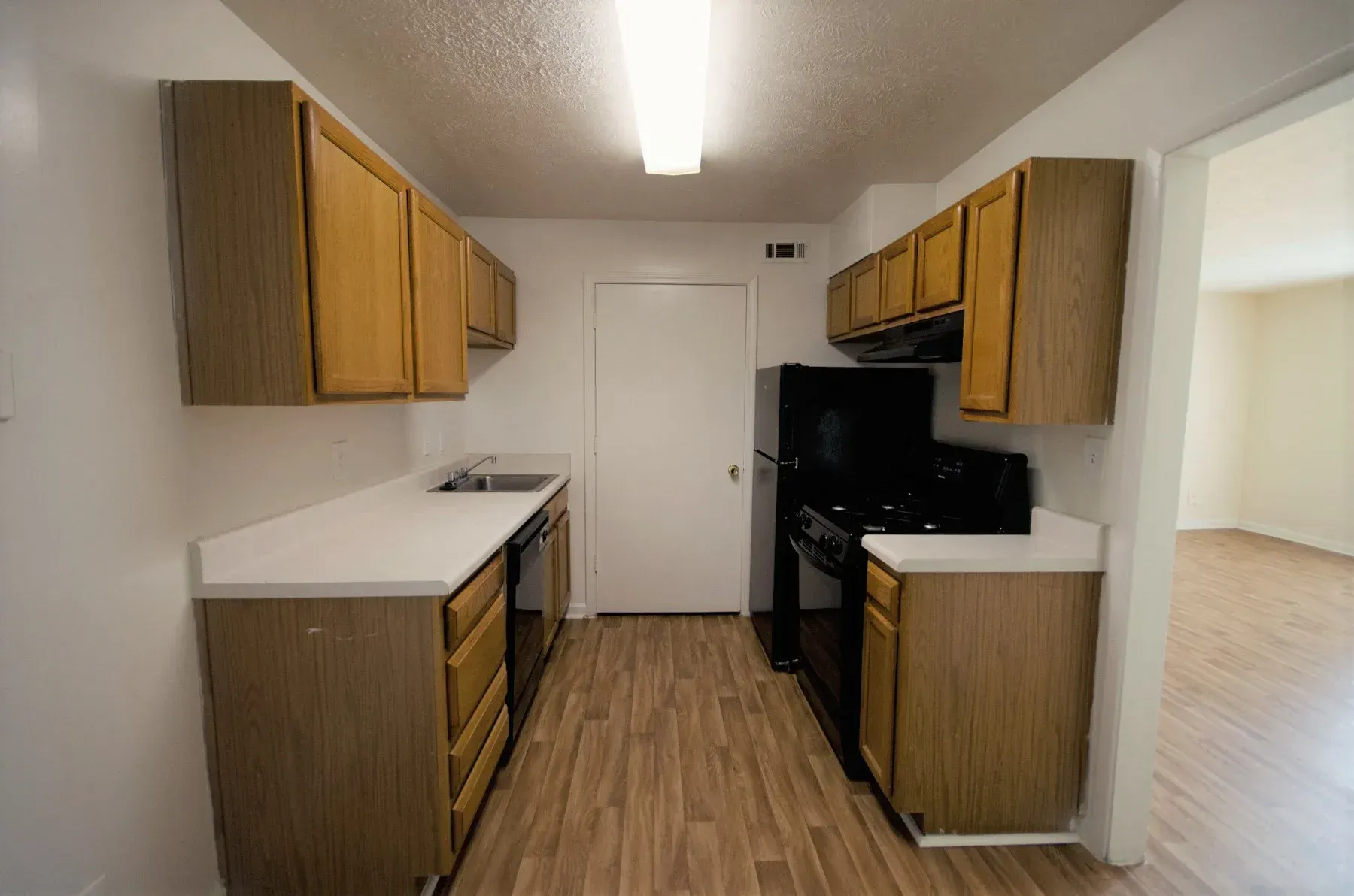 Kitchen with light-colored cabinets, white countertops, and black appliances. Door at the end, and a room on the right.
