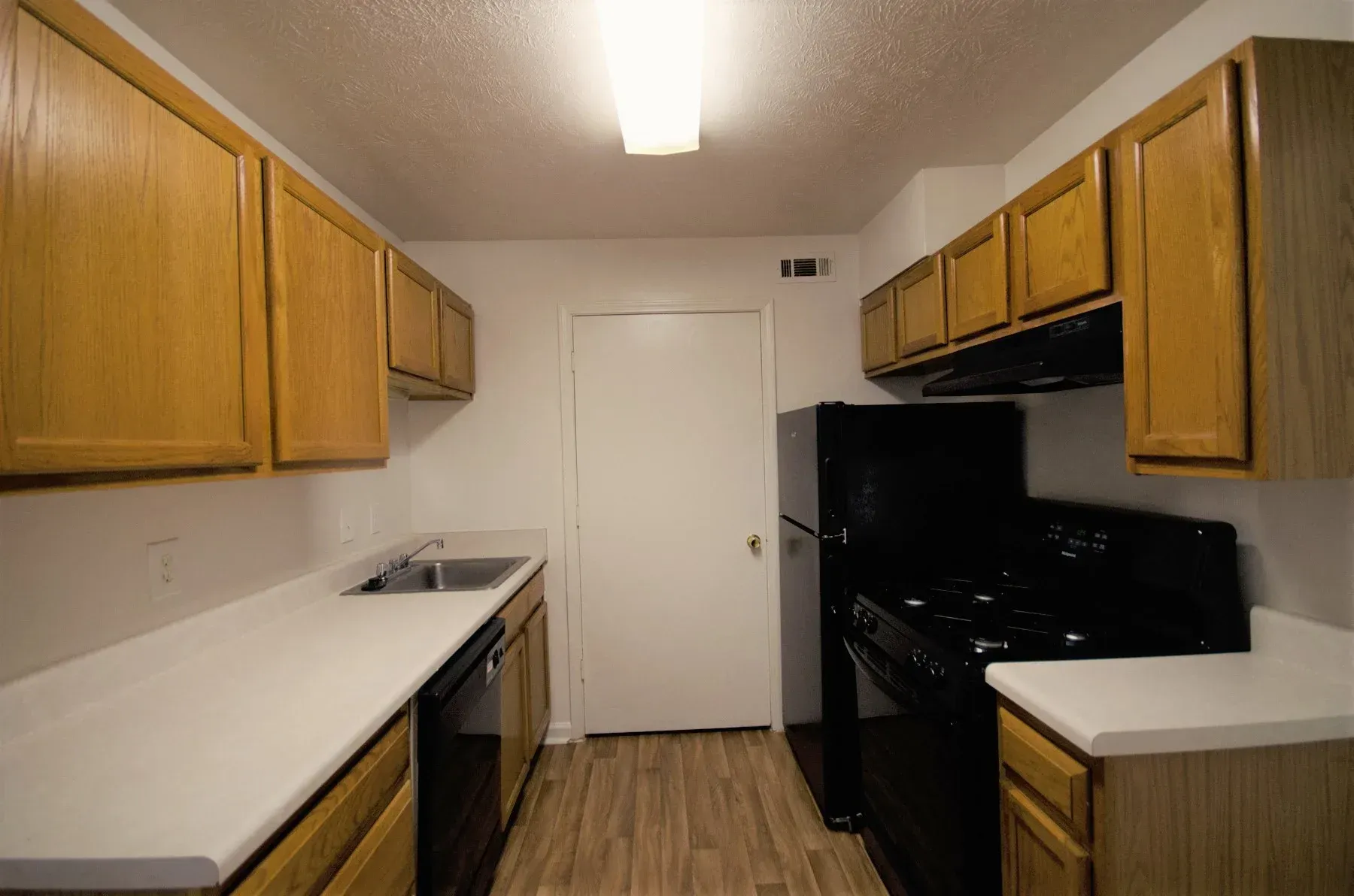 Kitchen with wooden cabinets, white countertops, black appliances, and a closed white door.