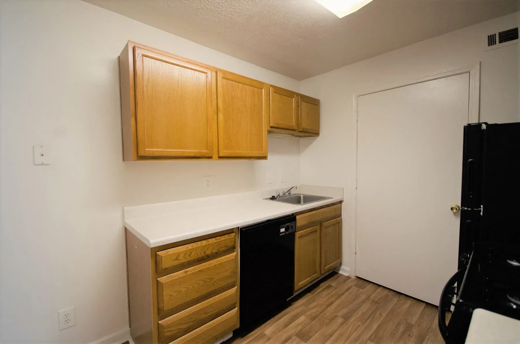 Kitchen with light wood cabinets, white countertops, black appliances, and white door.