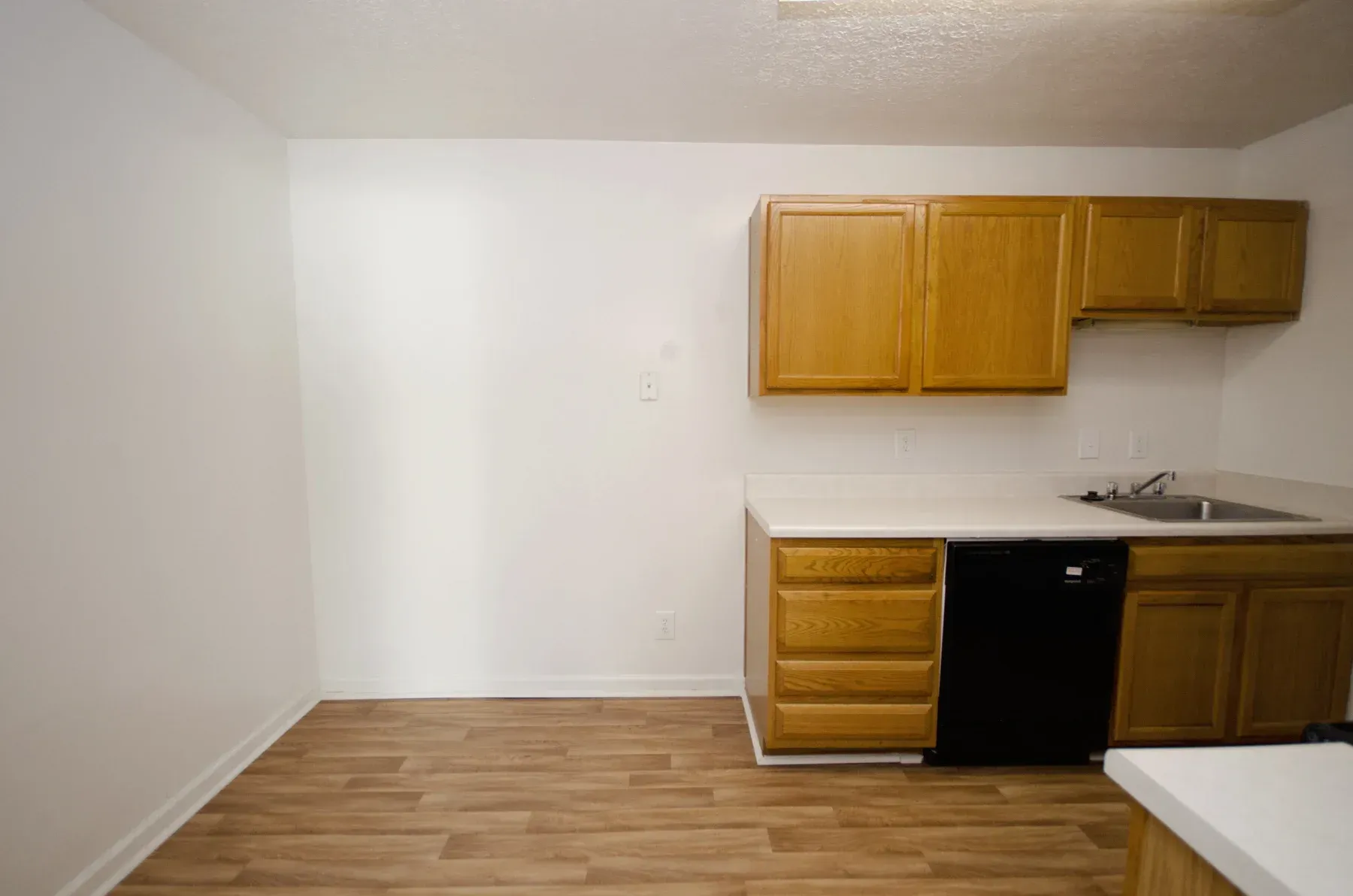 Kitchen with wood cabinets, white countertops, black dishwasher, and laminate flooring.