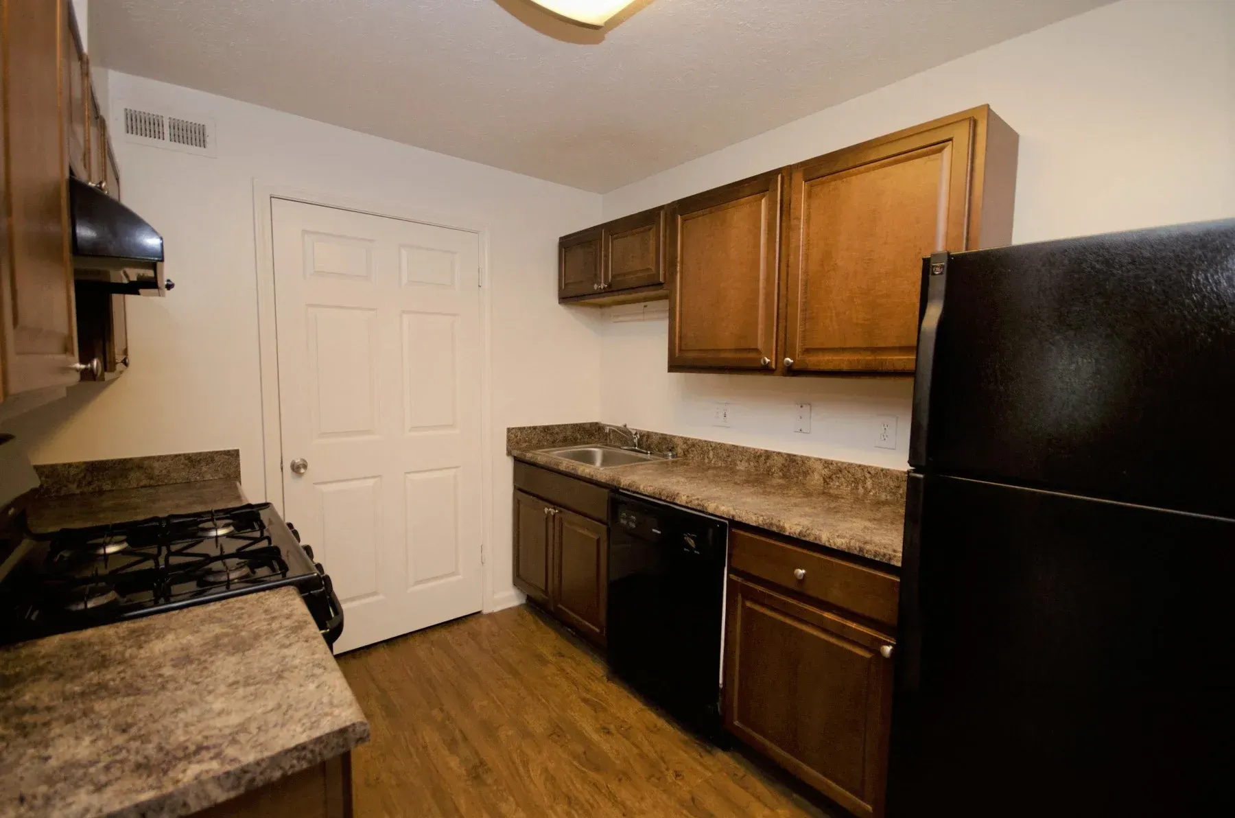 Kitchen with brown cabinets, black appliances, and a light-colored countertop and flooring.