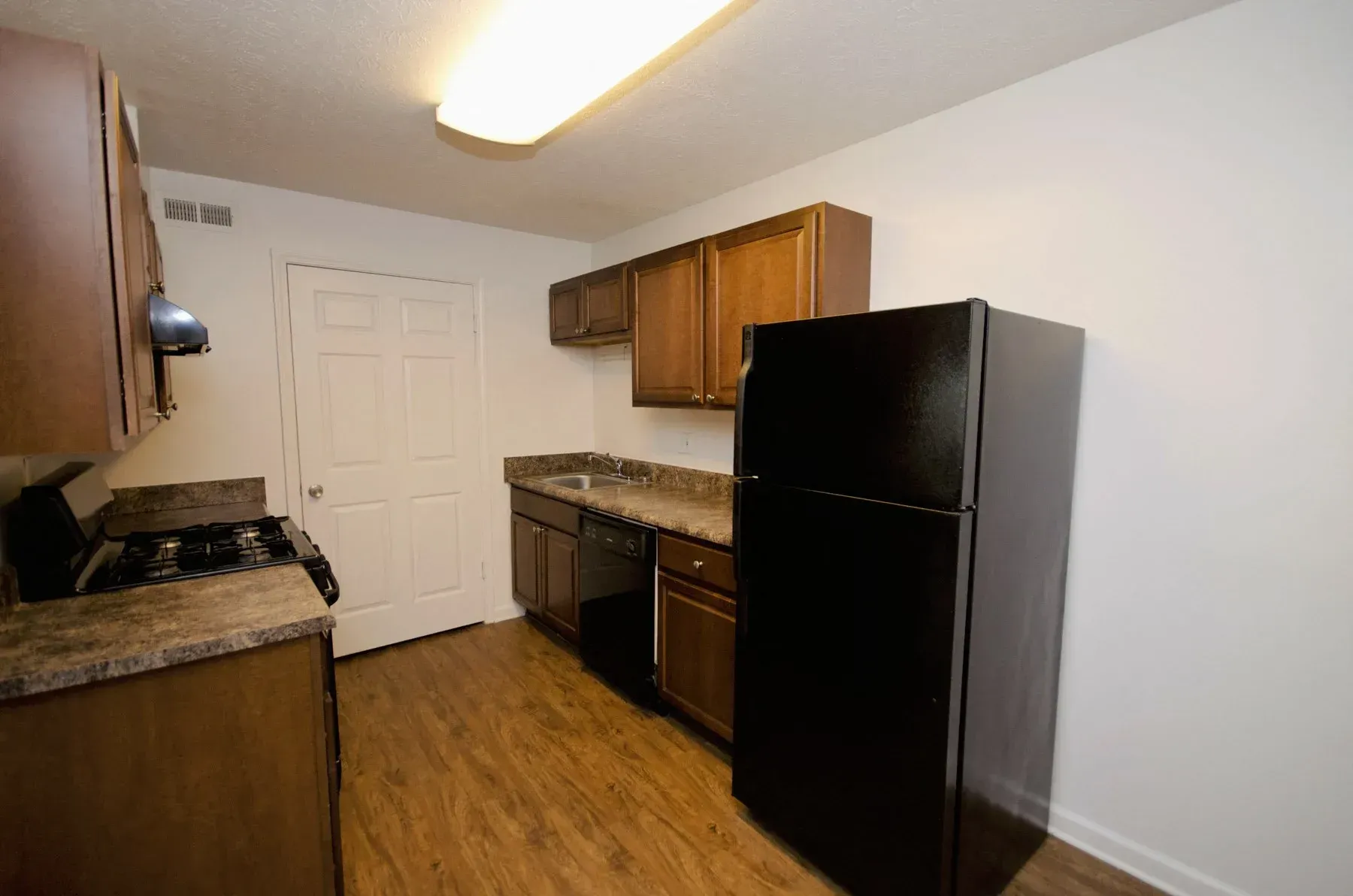 Kitchen with brown cabinets, black refrigerator, and wood-look flooring.