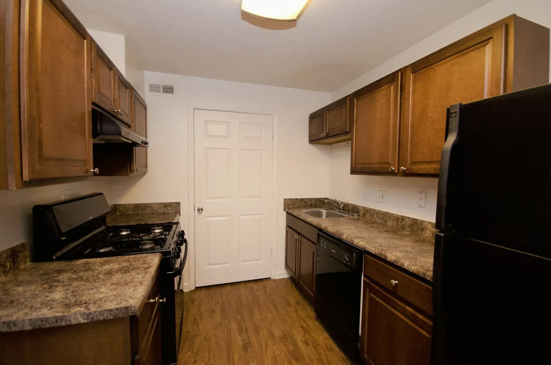 Kitchen with brown cabinets, black appliances, and a white door.