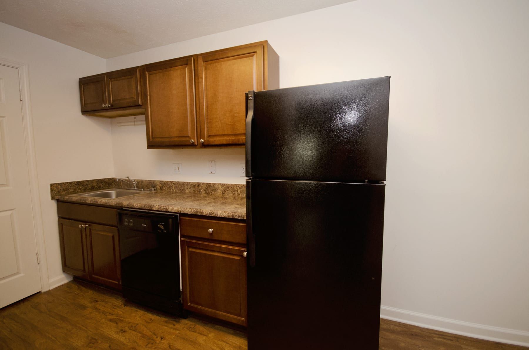 Kitchen with dark cabinetry, black refrigerator, countertop, and wooden floor.