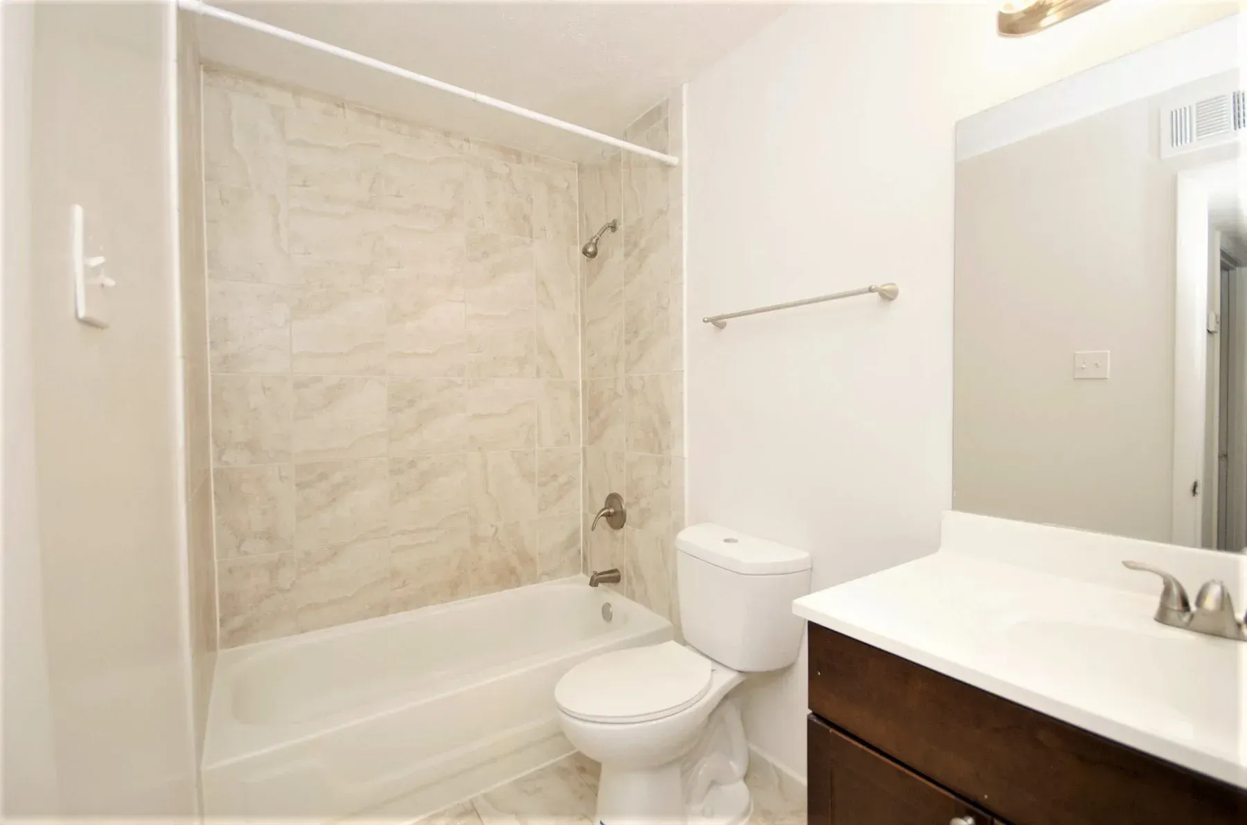 Bathroom with white walls, tiled shower, toilet, dark brown vanity, and mirror.