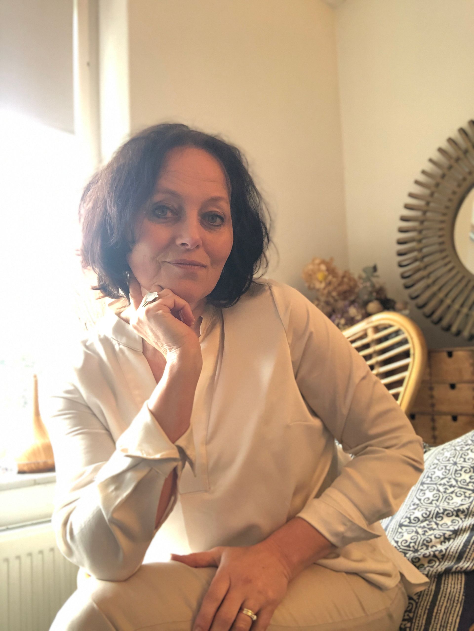A woman in a white shirt is sitting in a chair with her hand on her chin.