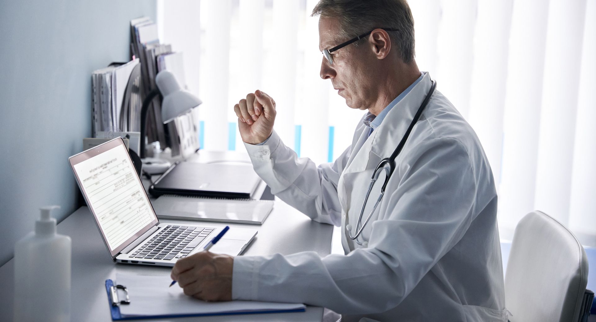 A doctor is sitting at a desk using a laptop computer.
