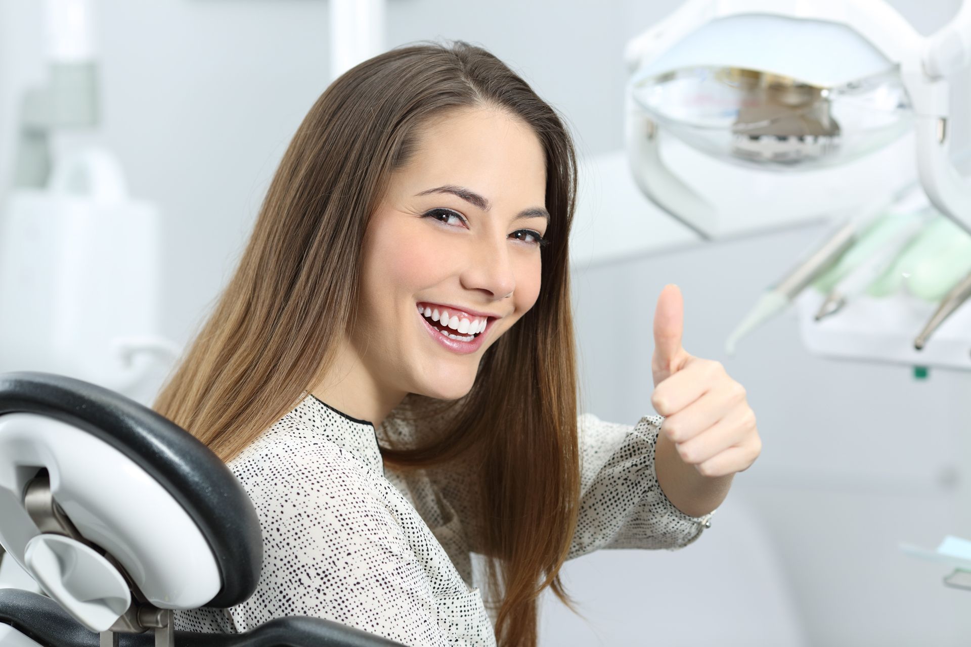 A woman is sitting in a dental chair and giving a thumbs up.