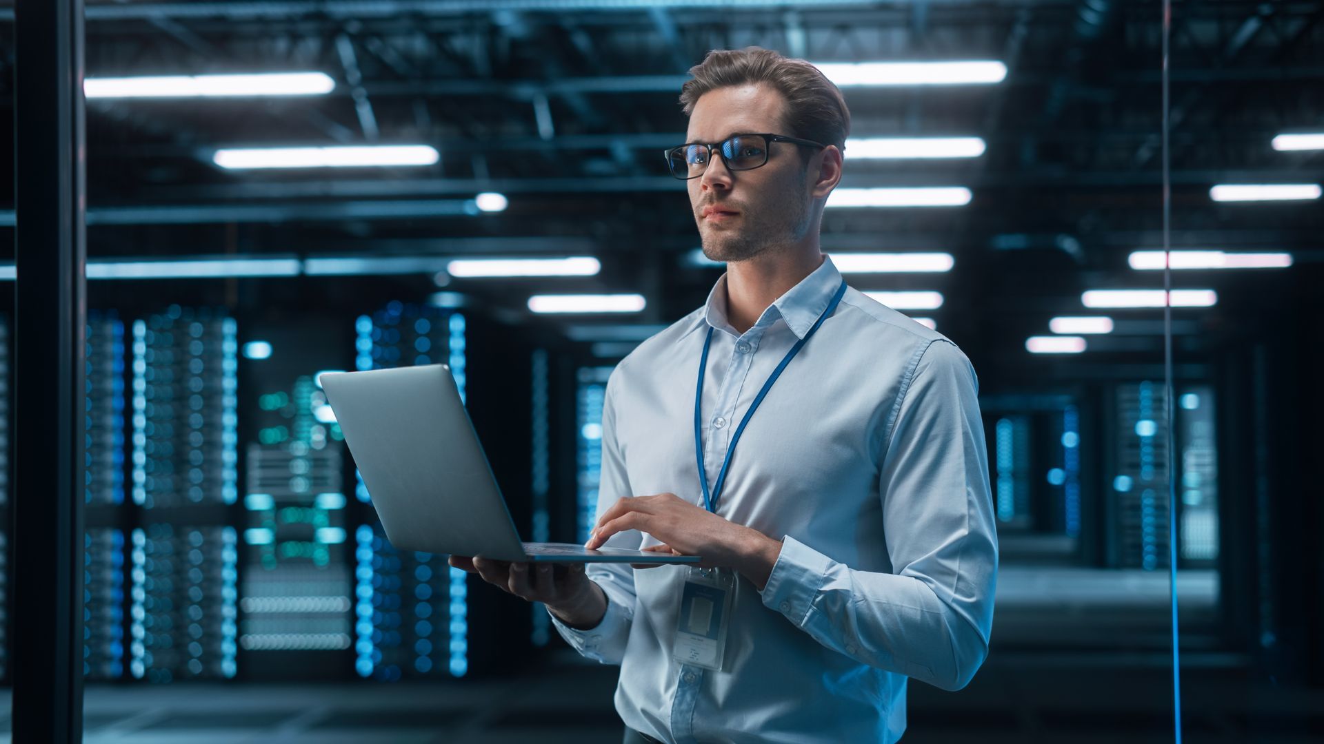 A man is using a laptop computer in a server room.